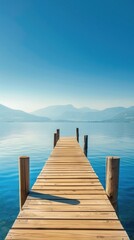 Naklejka premium Wooden dock extending into a clear blue lake with mountains in the background.