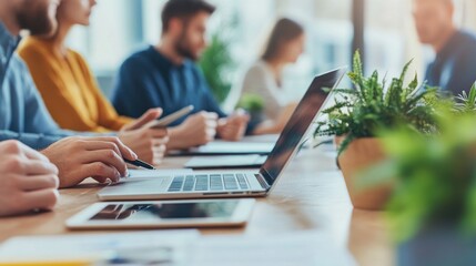 Close-up of business professionals working together in a modern office environment. The team is engaged in a discussion, using laptops, tablets, and papers. The image captures the dynamic nature of