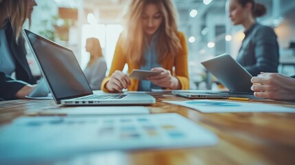 Close-up of business professionals working together in a modern office environment. The team is engaged in a discussion, using laptops, tablets, and papers. The image captures the dynamic nature of