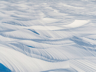 Snow texture. Wind sculpted patterns on snow surface. Wind in the tundra and in the mountains on the surface of the snow sculpts patterns and ridges (sastrugi). Arctic, Polar region. Winter background