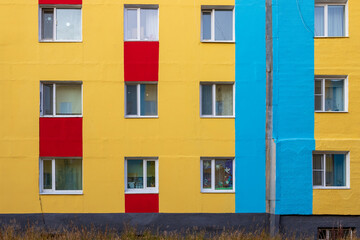 Facade of a colorful multi-colored building. The wall of the building is painted yellow, blue and red. Windows of an apartment building.