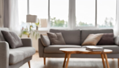 Blurred interior of light living room with grey sofas, coffee table and big window