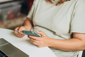Cropped unrecognizable woman doing online shopping over laptop with credit card and phone at desk in home office. One woman is buying online on her laptop