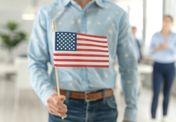 Close up of an American flag being held in the style of one person in the foreground, blurred people holding US flags and dressed in business casual standing behind him in a blurry background.