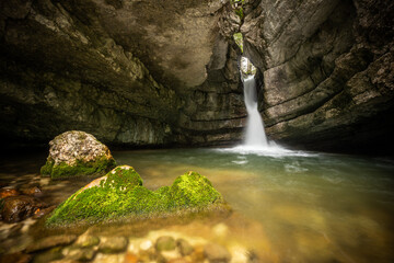 Serene Waterfall Cascading Through Rocky Outcrop Surrounded by Lush Green Mossy Stones in Tranquil Forest Setting