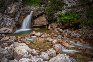 Serene Waterfall Cascading Over Rocks in Lush Green Forest During Daylight Hours