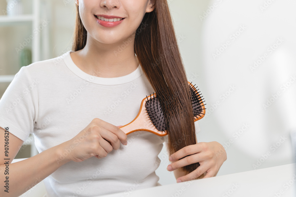 Wall mural happy asian woman brushing hair by wooden comb in the morning.