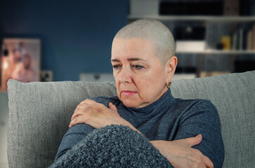 The image shows a woman with a shaved head, indicative of cancer treatment, sitting alone and...