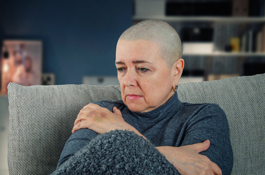 The image shows a woman with a shaved head, indicative of cancer treatment, sitting alone and seemingly lost in thought. The setting and her expression suggest a deep sense of loss and despair.