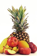 Assorted fresh fruits displayed artistically on a light background with pineapple, bananas, apples, and orange