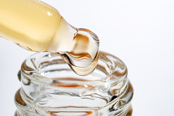macro shot of serum dropper pipette and pouring retinol beauty serum on white. Skin care treatment...