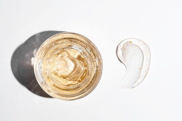 top view of glass jar and a smear of 24k gold cream gel for skin care on white background. Luxury cosmetics presentation