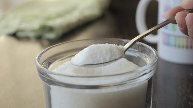 Slow Motion Act of Scooping Pure White Sugar With Spoon. Taking Teaspoon of Sugar From Glass Sugar Bowl. Sweets Addiction Junk Food. Concept of Unhealthy Eating, Diabetes, Obesity, Heart Disease. 