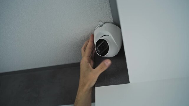 Professional male installer screws CCTV camera to the ceiling in office room using screwdriver tool and adjusts the angle. Monitoring and tracking. Video surveillance, security system, and privacy.