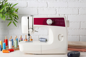 Modern sewing machine and craft accessories on wooden table near white brick wall