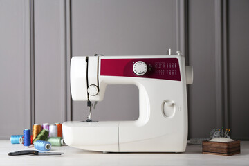 Sewing machine and craft accessories on white wooden table near gray wall