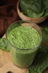 Tasty green smoothie in glass and spinach on table, closeup