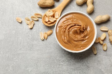 Tasty peanut butter in bowl and groundnuts on grey textured table, flat lay. Space for text
