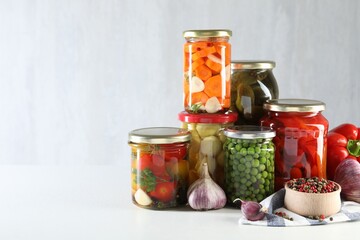 Jars with tasty pickled vegetables, mushrooms and spices on white background, space for text