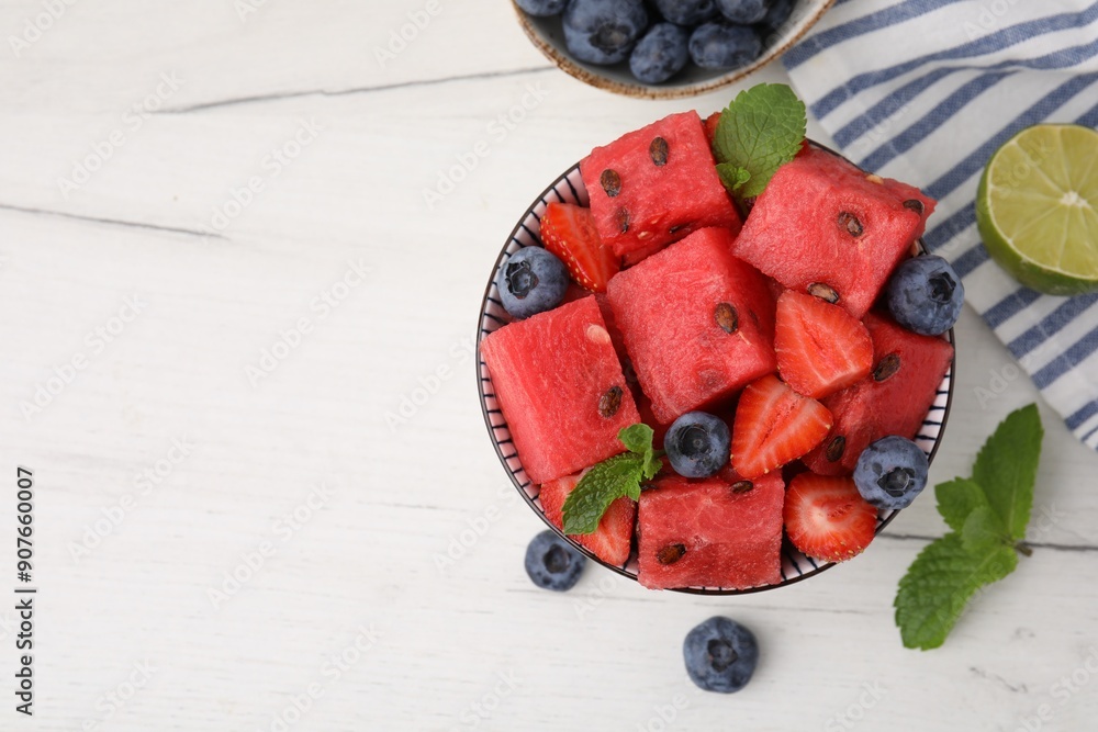 Poster Pieces of tasty watermelon, strawberries, blueberries and mint in bowl on white wooden table, flat lay. Space for text