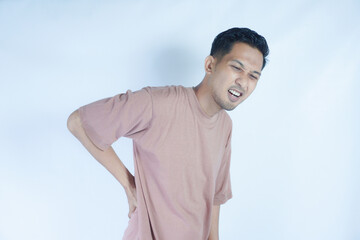 A man in a pink shirt bends over slightly and holds his lower back with a pained expression,...