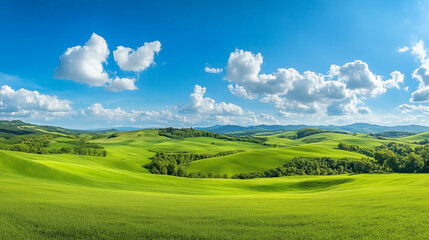 Fototapeta premium Panoramic view of vast green hills and meadows stretching out under a bright blue sky dotted with white, fluffy clouds.