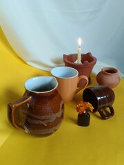 brown still life with mugs and a lightning candle near a white cloth. 