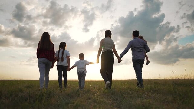 Large group of people in park walking at sunset. Family unity holding hands. Scenic outdoor lifestyle concept. Back view of diverse group in park. Togetherness concept in nature. Happy people in park.