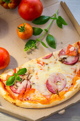 cooked pizza with salami and sausage in a box on a wooden table