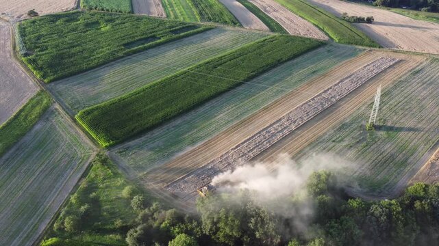 Drohne fliegt an Freileitung durch Agrarland mit M&auml;hdrescher bei der Getreideernte, Luftaufnahme