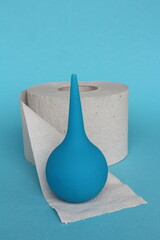 Blue syringe and roll of toilet paper on a blue background.