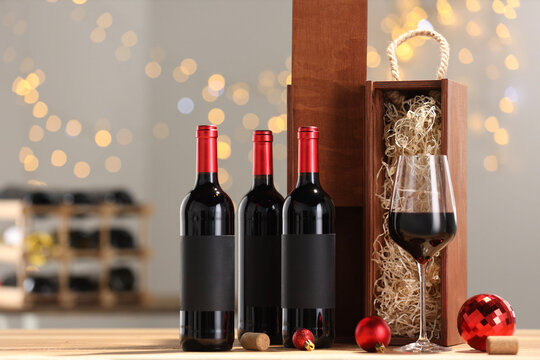 Bottles of wine, glass, wooden gift boxes, corks and red Christmas balls on table, space for text