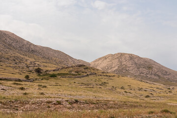 Panoramic view of rolling hills and rugged mountains peaks covered in  patchwork of golden grasslands and sparse vegetation in Vela Luka bay on island Otok Krk, Primorje-Gorski Kotar, Croatia. Hiking