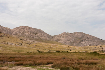 Fototapeta premium Panoramic view of rolling hills and rugged mountains peaks covered in patchwork of golden grasslands and sparse vegetation in Vela Luka bay on island Otok Krk, Primorje-Gorski Kotar, Croatia. Hiking