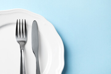 Stylish silver cutlery and plate on light blue background, top view. Space for text