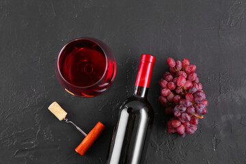 Corkscrew, glass of wine, bottle and grapes on black table, flat lay