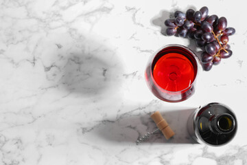 Corkscrew, glass of wine, bottle and grapes on white marble table, flat lay. Space for text