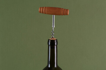 Wine bottle with corkscrew on olive background, closeup