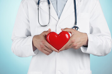 Doctor with red heart on light blue background, closeup