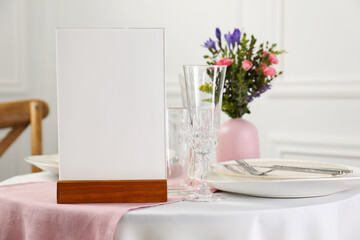Menu holder, clean dishware and vase with beautiful flowers on white table in restaurant