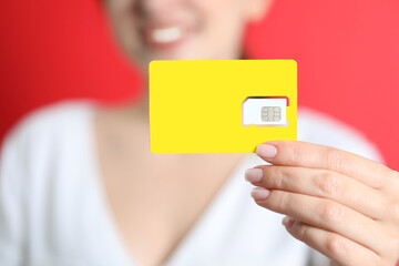 Woman holding SIM card on red background, closeup