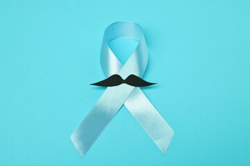Light blue ribbon and fake mustache on color background, top view. Prostate cancer awareness