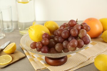 Fruit vase with grapes and lemon on wooden table in kitchen, closeup
