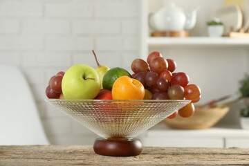 Glass vase with different fresh fruits on wooden table