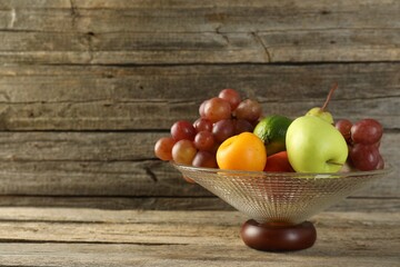 Glass vase with different fresh fruits on wooden table, space for text