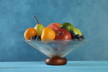 Glass vase with different fresh fruits on light blue wooden table