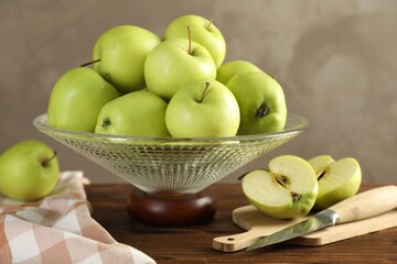 Glass vase with fresh green apples, cutting board and knife on wooden table against gray background, closeup