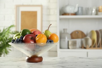 Glass vase with different fresh fruits on white marble table. Space for text