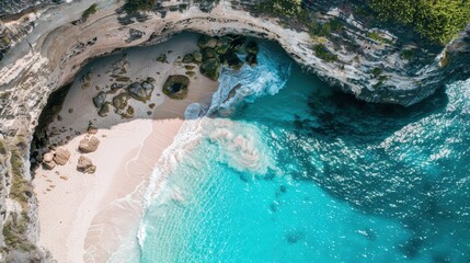 Turquoise water is seen crashing on a secluded beach with white sand under a large cliff
