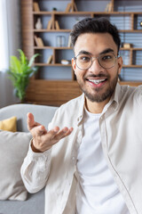 Vertical close-up photo of a young Indian man in casual clothes who is at home, recording a video,...